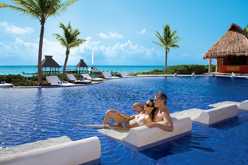 Couple lounging on in-pool chaise lounge overlooking ocean