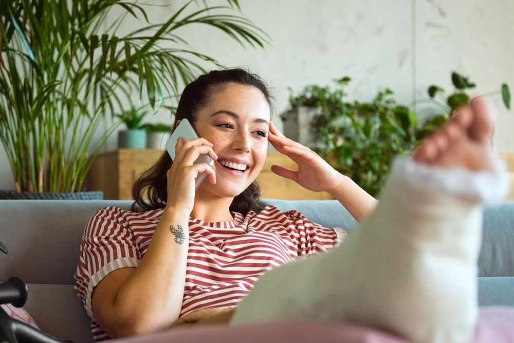 Young woman in a leg cast speaking on a mobile phone