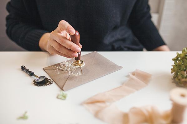 Man using wax seal to close wedding invitation envelope