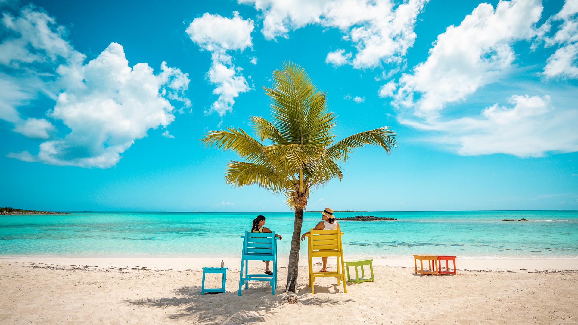 Women sitting in colorful lifeguard chairs on a tropical beach