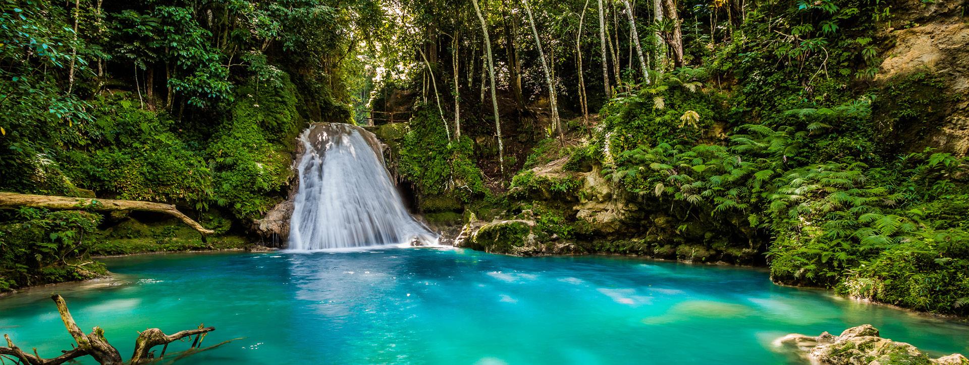 Waterfall flowing into a clear blue swimming hole in Jamaica