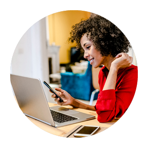 A woman works on her computer with a mobile phone in hand