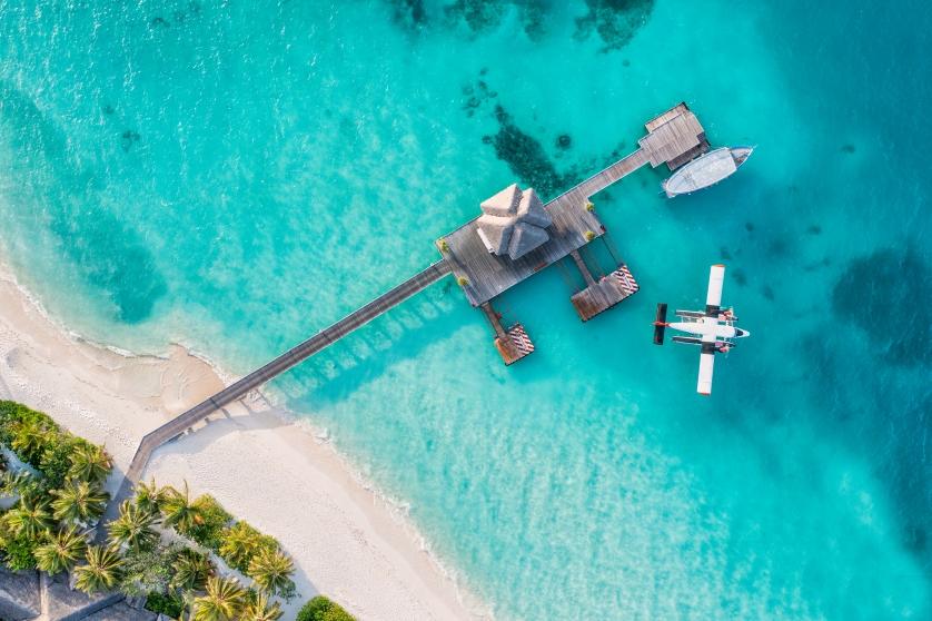 Beautiful aerial view of Maldives shore, pier villa seaplane top view, wooden boat Dhoni and tropical beach.